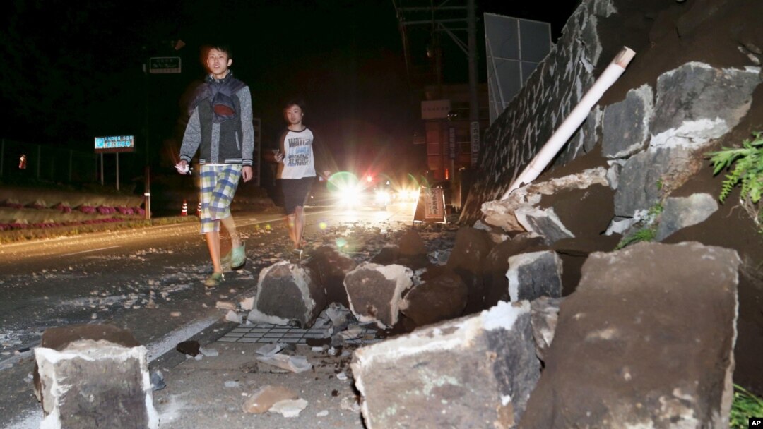 Warga berjalan di dekat tembok yang runtuh di kota Mashiki, Kumamoto, Jepang selatan pasca gempa Kamis malam (14/4).