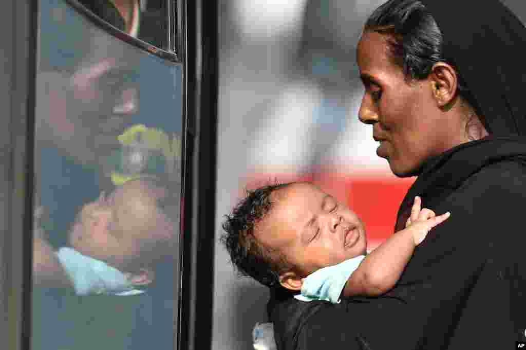 A woman carries a baby as she boards a bus after disembarking from the Italian Coast Guard ship Fiorillo in the harbor of Pozzallo, near Ragusa, Sicily. On Thursday, 381 people were saved by the Italian coast guard before their boat sank off the Libyan coast.