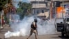 FILE - A police officer runs away from tear gas during a protest to demand the resignation of Haiti's president Jovenel Moise in Port-au-Prince, Haiti, Feb. 10, 2021. 