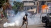 A police officer runs away from tear gas during a protest to demand the resignation of Haiti's President Jovenel Moise in Port-au-Prince, Haiti, Feb. 10, 2021. 