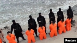 FILE - Captives in orange jumpsuits — purported to be Egyptian Christians —kneel in front of armed Islamic State militants along a beach said to be near Tripoli, in this still image from an undated video made available on social media, Feb. 15, 2015.