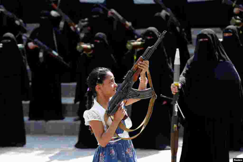 A girl holds a rifle in front of women loyal to the Houthi movement, who are taking part in a parade to show support for the movement in Sana'a, Yemen.