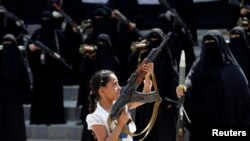 Seorang perempuan memegang senjata di depan perempuan-perempuan yang setia kepada gerakan Houthi yang ikut dalam parade dukungan di Sana'a, Yaman, 6 September 2016. 