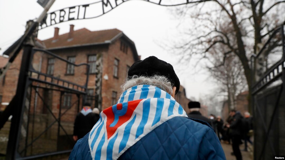 Para penyintas dan tamu berjalan melewati gerbang bekas kamp konsentrasi dan pemusnahan Nazi bertuliskan"Arbeit Macht Frei" ("Bekerja Membebaskan Anda") Auschwitz, dalam acara peringatan 73 tahun pembebasan kamp dan korban Holocaust, di Oswiecim, Polandia, 27 Januari 2018.