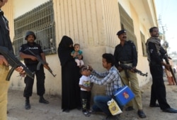 FILE - Pakistani policeman stand guard as a health worker administers polio drops to a child during a polio vaccination campaign after a day of an attack by gunmen in Karachi on April 21, 2016.