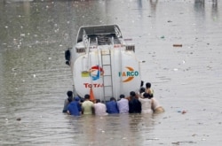 FILE - Men push a truck through a flooded road during monsoon rain, in Karachi, Pakistan, Aug. 25, 2020.