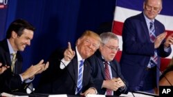 President Donald Trump smiles as people applaud him during a round-table discussion on tax policy, April 5, 2018, in White Sulphur Springs, W.Va. From left are Rep. Evan Jenkins, R-W.Va., West Virginia Attorney General Patrick Morrisey, and CEO of Davis Trust Company Hugh Hitchcock.