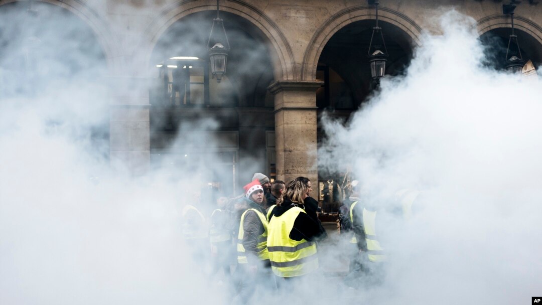 Para demonstran (mengenakan rompi kuning) berjalan melewati bom asap di dekat kebun Tuileries di Paris, Sabtu, 22 Desember 2018. (Foto: dok).