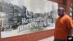 Freeman Culver berdiri di depan mural yang berisi daftar nama-nama usaha yang hancur saat pembantaian rasial warga kulit hitam di Kota Tulsa pada 1921, di Tulsa, Oklahoma, 15 Juni 2020. (Foto: AP)