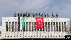 FILE - Turkish soldiers, right, and Turkey-backed opposition fighters stand atop a building next to their flags in Ras al Ayn, northeastern Syria, Oct. 23, 2019. 