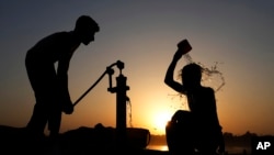 A Pakistani youth, right, cools off under a hand pump at sunset during hot weather in Lahore, Pakistan, May 28, 2024. 