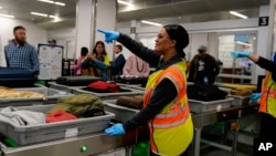 A worker points as people wait for the belongings at the Transportation Security Administration security area at the Hartsfield-Jackson Atlanta International Airport on Wednesday, Jan. 25, 2023, in Atlanta. (AP Photo/Brynn Anderson)