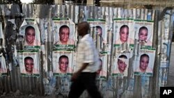 A man walks past a corrugated fence covered with election posters in Port-au-Prince, Haiti, Mar 16 2011