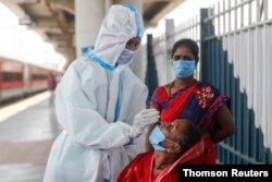 A healthcare worker in personal protective equipment collects a swab sample from a woman, amidst the spread of the coronavirus disease, at a railway station in Mumbai, India, April 16, 2021.
