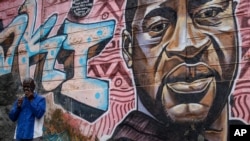 A local resident stands next to a mural showing George Floyd with the Swahili word "Haki" or "Justice" in the Kibera low-income neighborhood of Nairobi, Kenya, April 21, 2021.