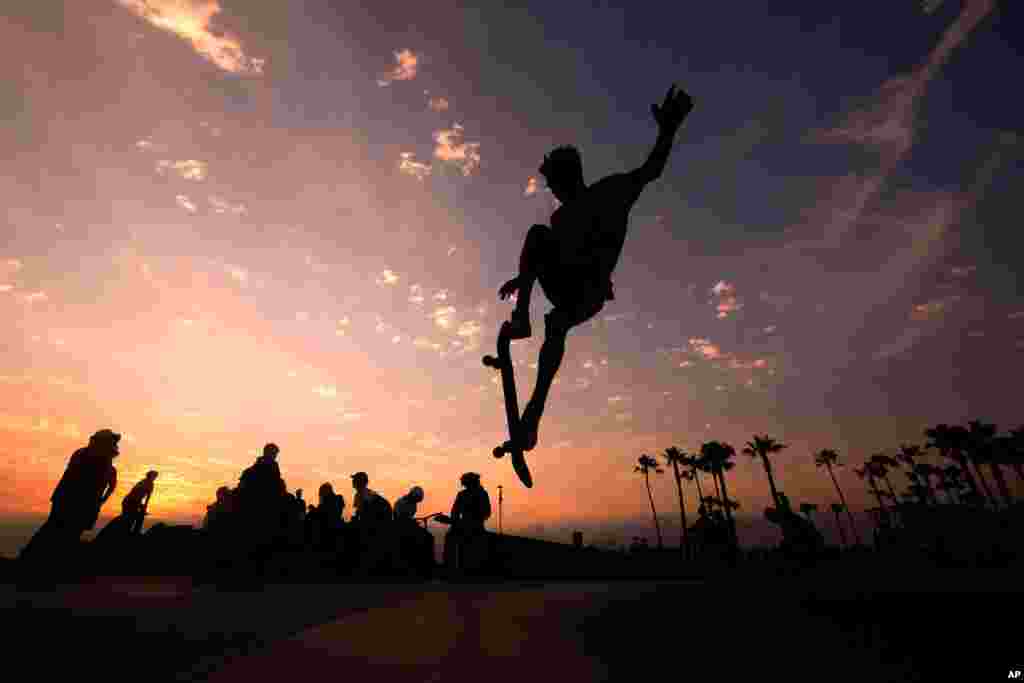 A skateboarder is silhouetted as he jumps high at the skateboard park during sunset, June 16, 2021, in Venice Beach, Los Angeles, California.