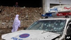 A Pakistani woman walks past a police vehicle hit by a roadside bombing in Charsadda near Peshawar, Pakistan, March 31, 2011