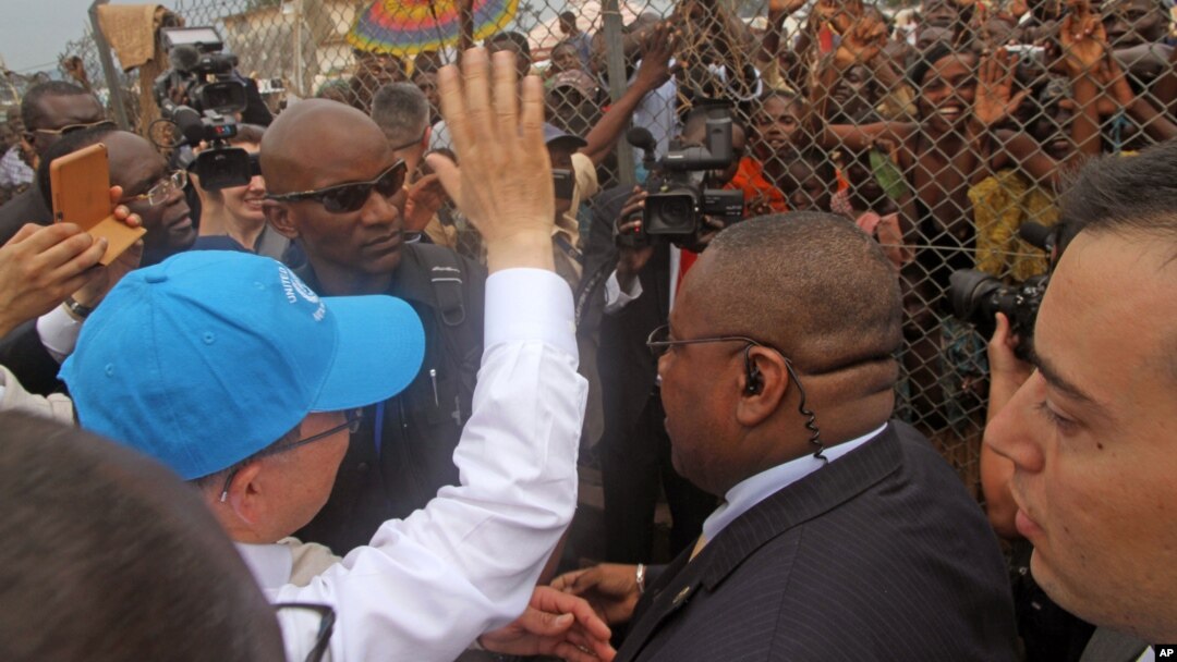 U.N. Secretary-General Ban Ki-moon, in a cap, waving at people kept back by a wire fence, as he walks surrounded by U.N. security personnel in a secured location in Bangui, Central African Republic, April 5, 2014.