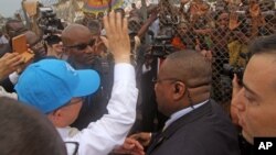 U.N. Secretary-General Ban Ki-moon, in a cap, waving at people kept back by a wire fence, as he walks surrounded by U.N. security personnel in a secured location in Bangui, Central African Republic, April 5, 2014.