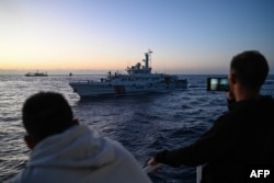 Philippine coast guard personnel film a China coast guard vessel during a supply mission in the disputed South China Sea on March 5, 2024. Philippine officials say China coast guard vessels caused two collisions with Philippine boats and directed a water cannon at one of them.