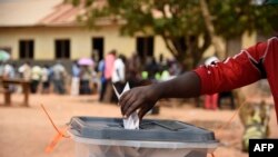 Un homme dépose son bulletin de vote alors que des personnes qui n'ont pas pu voter le premier jour du scrutin font la queue devant les bureaux de vote dans le district de Wakiso, en Ouganda, le 19 février 2016.