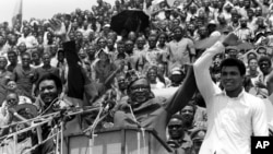 Le président du Zaïre (devenu RDC), Mobutu Sese Seko, au centre, soulève la main de Mohamed Ali, à droite, et de George Foreman, à gauche, sous les acclamations des dizaines de zaïrois réunis au stade du 20 Mai (rebaptisé Tata Raphaël) quelques jours avant le combat du championnat mondial de boxe entre les deux boxeurs poids-lourds, à Kinshasa, Zaïre (RDC), 17 septembre 1974. (AP Photo)