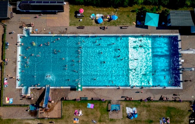 People spend time in a public pool in Wehrheim near Frankfurt, Germany, on a hot Saturday, July 8, 2023. (AP Photo/Michael Probst)