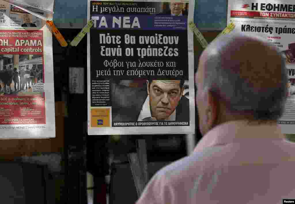A man reads the front pages of various newspaper hanging at a kiosk in Athens, June 29, 2015. 