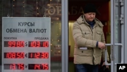 FILE - A man leaves a bank next to an exchange sign showing the currency exchange rates in Moscow, Dec. 20, 2024. 