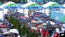Visitors line up to enter the Winter Games venues on opening day. Umbrellas were plentiful, snow was not