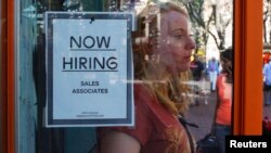 FILE - A woman walks past a 'Now Hiring' sign as she leaves the Urban Outfitters store at Quincy Market in Boston, Massachusetts.