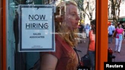 FILE - A woman walks past a 'Now Hiring' sign as she leaves the Urban Outfitters store at Quincy Market in Boston, Massachusetts, Sept. 5, 2014. 