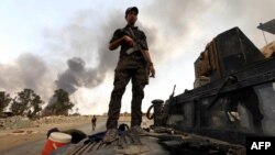 A member of the Iraqi government forces stands on a military vehicle as smoke billows from oil wells, set ablaze by Islamic State (IS) group militants before fleeing the oil-producing region of Qayyarah, Aug. 30, 2016.