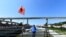 FILE - A man stands next to flowers and a t-shirt with the picture of a victim of the collapse of the Morandi bridge, as static testing operations are performed on the bridge ahead of its inauguration, in Genoa, Italy, July 19, 2020.