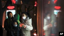 FILE - Commuters wearing protection masks, wait for buses at a bus station on a heavy polluted day in Beijing, China.