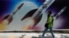 (FILE) A woman walks past a banner showing missiles being launched, in northern Tehran, Iran, Friday, April 19, 2024.