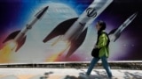 Một người phụ nữ đi ngang qua biểu ngữ có hình tên lửa đang được phóng, ở phía bắc Tehran của Iran hôm 19/4.