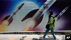(FILE) A woman walks past a banner showing missiles being launched, in northern Tehran, Iran, Friday, April 19, 2024.