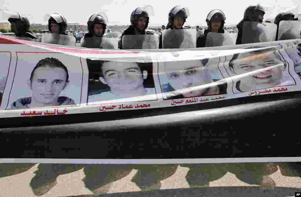 Riot police line up behind a banner with pictures of men killed during the revolution carried by anti-Mubarak protesters, outside the Police Military Academy complex in Cairo, during the trial session of ousted President Hosni Mubarak. (AP Image)