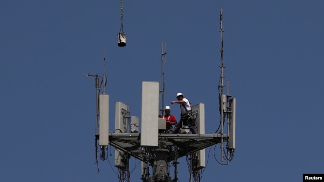 Workers install 5G telecommunications equipment on a T-Mobile tower in Seabrook, Texas, May 6, 2020.