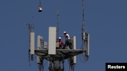 Workers install 5G telecommunications equipment on a T-Mobile tower in Seabrook, Texas, May 6, 2020.