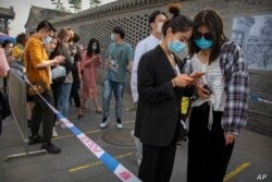 Personas usando máscaras usan sus celulares inteligentes para introducir su información personal antes de entrar a un centro comercial en Beijing.