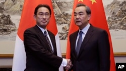 Menteri Luar Negeri Jepang Fumio Kishida (kiri) berjabat tangan dengan Menteri Luar Negeri China Wang Yi dalam pertemuan di Beijing (30/4). (AP/Jason Lee)