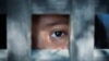 The blank stare of a child's eye who is standing behind what appears to be a wooden cage to convey captivity, or bondwoman. (File)