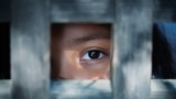 The blank stare of a child's eye who is standing behind what appears to be a wooden cage to convey captivity, or bondwoman. (File)