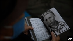 FILE - Holocaust survivor Shalom Stamberg holds a book with a photo of himself in Auschwitz just before the start of an annual Holocaust memorial ceremony, in Haifa, Israel, April 21, 2020. 