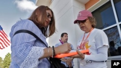 FILE - In this Dec. 10, 2019 photo, Hispanic Federation Canvasser Ana M. Vigo, right, registers Maria Moralez, left, to vote as Ivan Baez Munoz looks on outside the Polk Coutny Tax Collectors office in Davenport, Fla. 