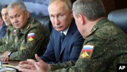 FILE - Umkhokheli wakwele Russia, uMnu. Vladimir Putin, okhokhela uhlangothi lwezomvikela, uMnu. Sergei Shoigu, labanye baxoxa ngezomvikela bese nkambeni eyeKapustin Yar, Russia.