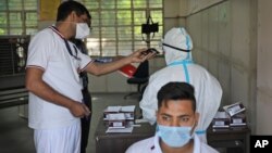A Delhi police volunteer holds a mobile phone for a health worker as she takes an urgent call during testing for COVID-19 in New Delhi, India, Saturday, 2020. 