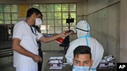 A Delhi police volunteer holds a mobile phone for a health worker as she takes an urgent call during testing for COVID-19 in New Delhi, India, Saturday, 2020. 